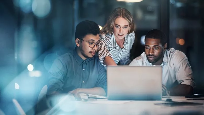 three young businesspeople working together on a laptop in their office late night