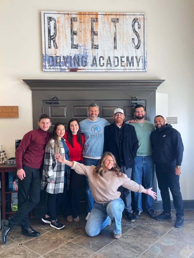 REETS Drying Academy team posing in front of the sign