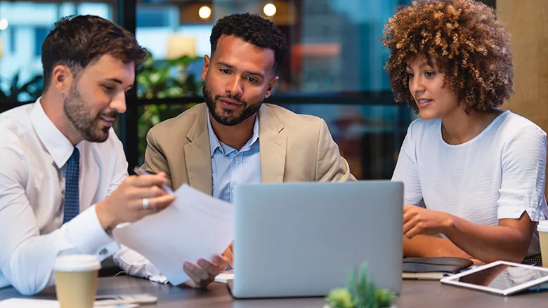 Three business people meeting and looking at a laptop and a document.