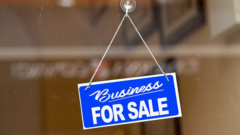 Blue sign hanging at the glass door of a shop saying: "Business for sale"