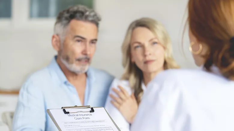 Doctor filling out medical insurance form with mature couple