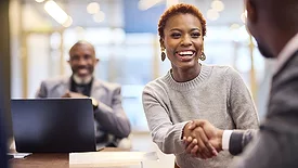 A smiling businesswoman shakes hands with a businessman during a meeting