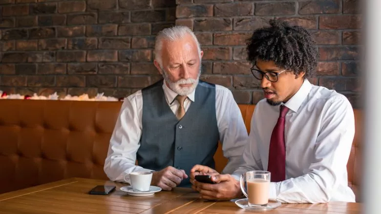 Two businessmen sitting in café looking at smart phone Two businessmen sitting in café looking at smart phone