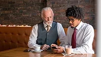 Two businessmen sitting in café looking at smart phone