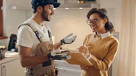 Smiling young woman signing document while communicating with handyman at the kitchen