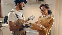 Smiling young woman signing document while communicating with handyman at the kitchen